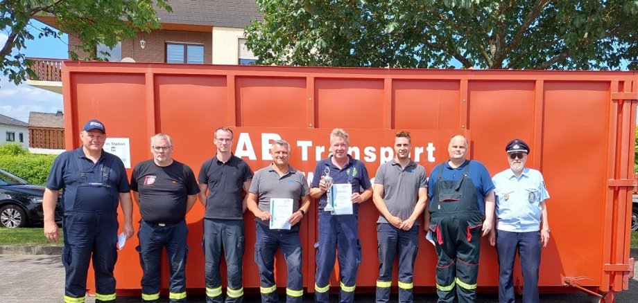 Acht Feuerwehrleute stehen vor Container mit Urkunden